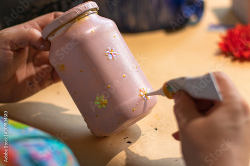 Female artist is using a glue on pink handmade glass can with a painting on it