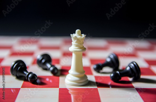 Symbolic shot on chess board. White queen stands tall with black pawns lying on floor