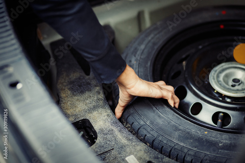 Close up mechanic hand taking spare tire at boot photo