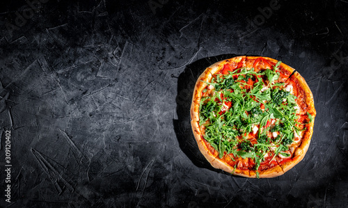 Tasty traditional italian pizza with salami, cheese, tomatoes greens on a dark background