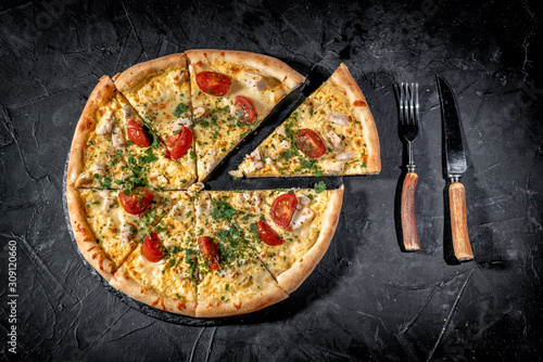 Tasty traditional italian pizza with salami, cheese, tomatoes greens on a dark background