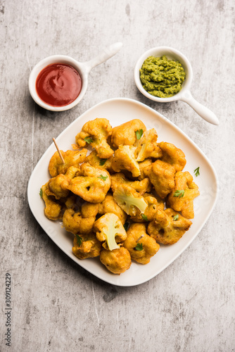 Gobi pakora or Phoolgobi pakoda made using fresh cauliflower dipped chickpea batter and then fried in oil. served with tomato ketchup and mint chutney. selective focus