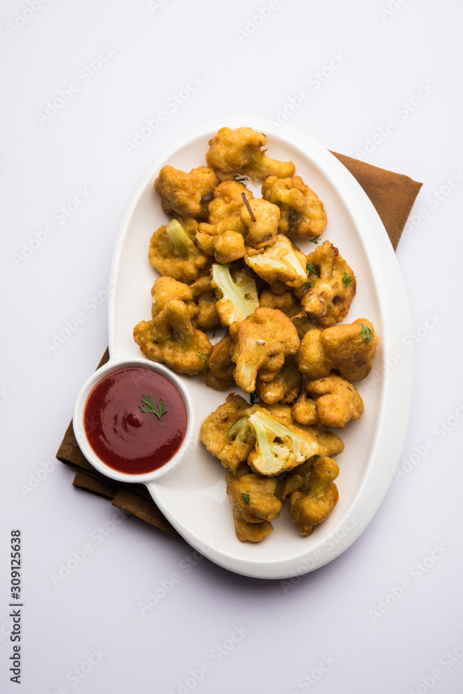Gobi pakora or Phoolgobi pakoda made using fresh cauliflower dipped chickpea batter and then fried in oil. served with tomato ketchup and mint chutney. selective focus