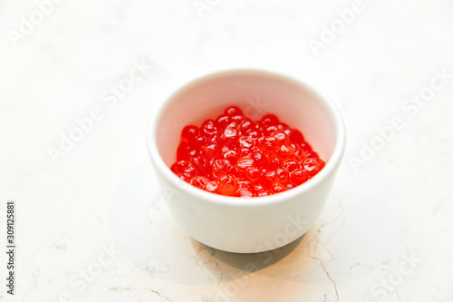 large Red caviar, in a white saucer, standing on a table on a white background