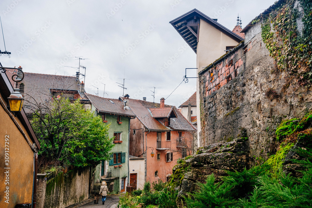 View of low townhouses of different colors with an old wall covered with moss in Annecy France. Photography of a narrow European street with old architecture.
