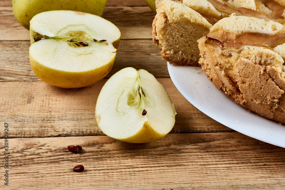 Sliced pieces of green apple next to a baked apple pie on a white plate on a wooden background