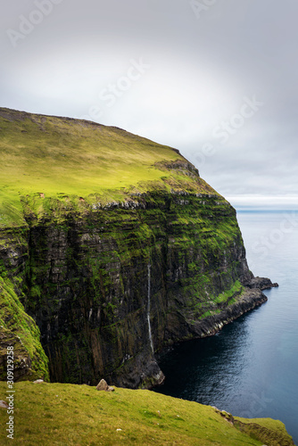 Waterfall falls into the ocean on hiking path in Gjogv village, Faroe Islands.