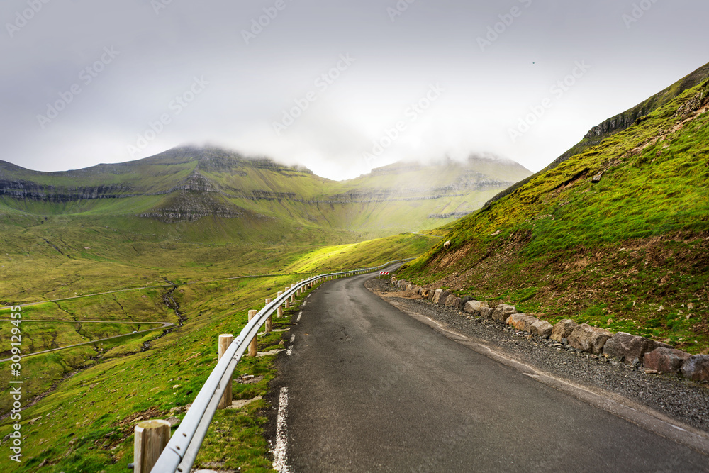 Road trip adventure photo with green mountains covered with overcast sky. Faroe Islands, Denmark.