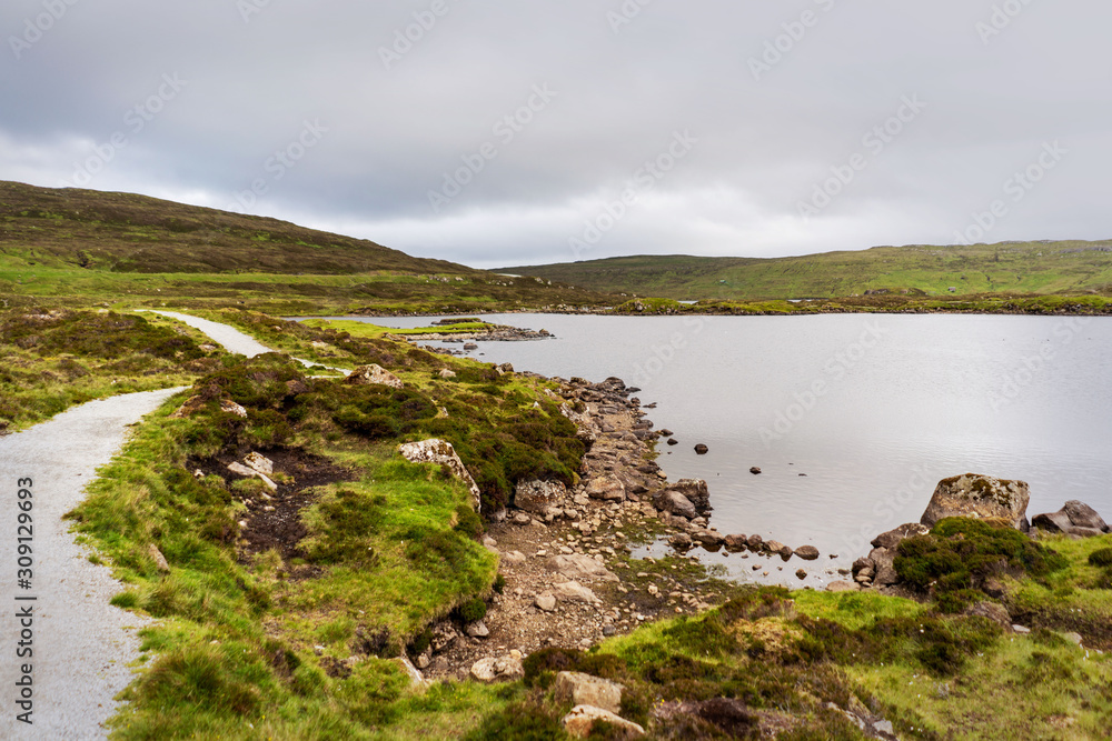 Lake mirror and green mountains around hiking path, Faroe Islands.