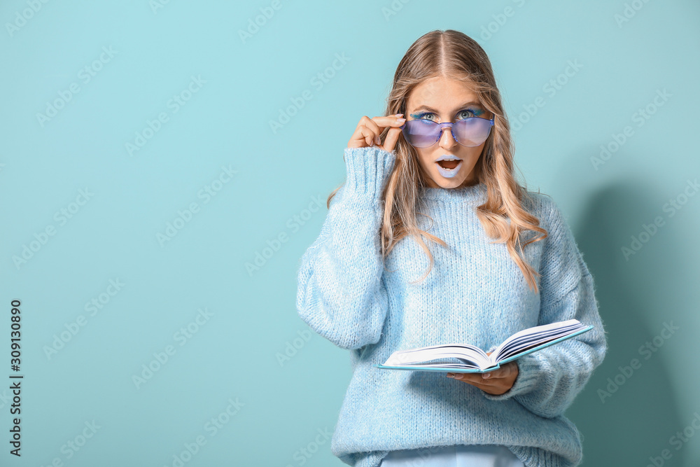 Fashionable surprised young woman with book on color background Fashionable surprised young woman with book on color background