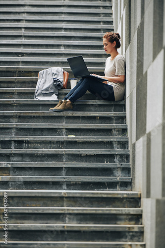 Young woman concentrated on work sitting on steps with laptop