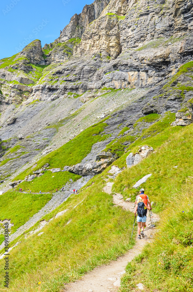 Hiking trail in the Swiss Alps photographed in the summer season. Tourists walking hiking path in the Kandersteg area, Switzerland. Steep mountains in the background. Green Alpine landscapes