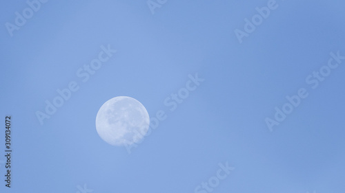 Distant view of the bright moon at dawn with a blue background © ArLawKa