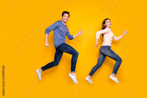 Full body profile side photo of funky brown red hair married couple jump run after sales discounts wear pink blue sweater sneakers isolated over yellow color background