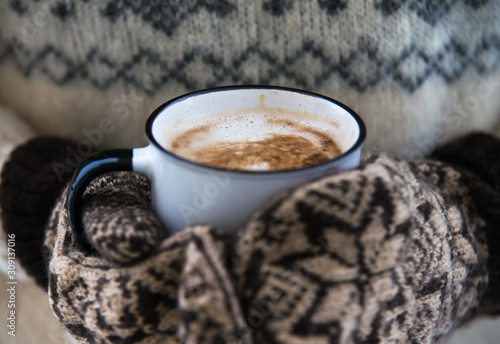woman is holding cup of coffee with milk in warm gloves