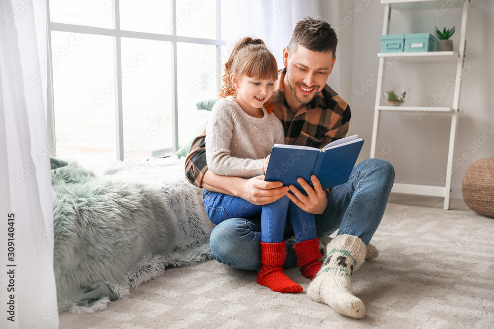 Cute little girl with father reading book at home