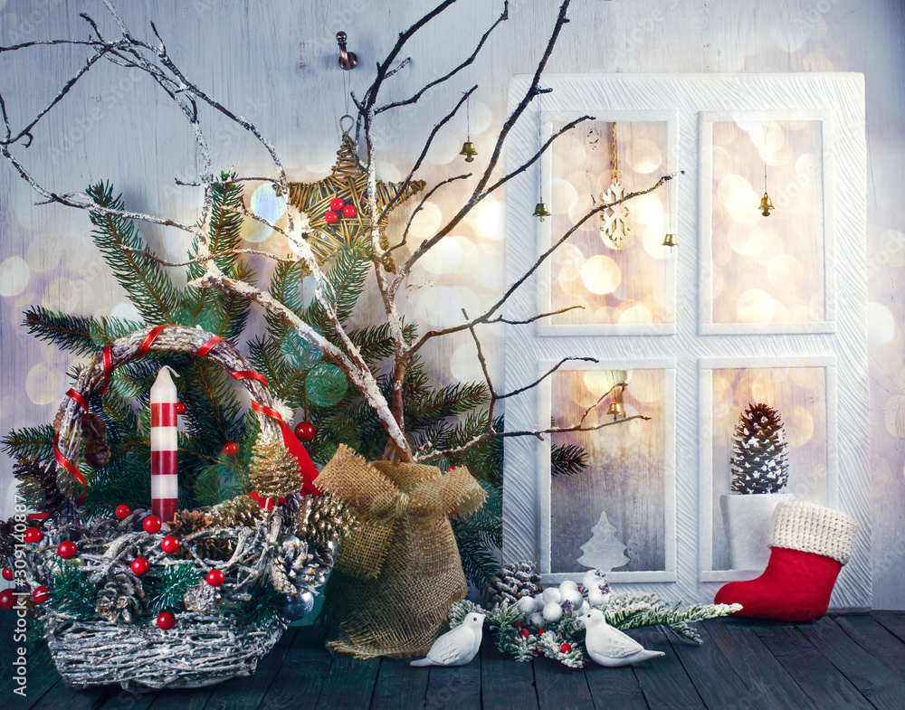 Obraz premium Christmas eve background with window, wicker festive basket, birds, candle, fir tree, pine, spruce cones, acorns on shabby wooden old table, New Year night winter holiday home natural material decor