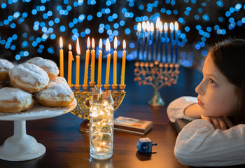 Child girl Looking at Menorah Candles on wooden table and sufganiyot on background light glitter bokeh overlay. Hanukkah jewish holiday Israel hebrew traditional family celebration invitation design