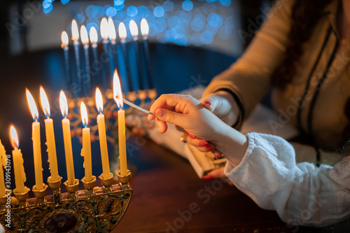 jewish holiday Chanukah/Hanukkah family selebration. Jewish festival of lights. Children lighting candles on traditional menorah over glitter shiny background photo