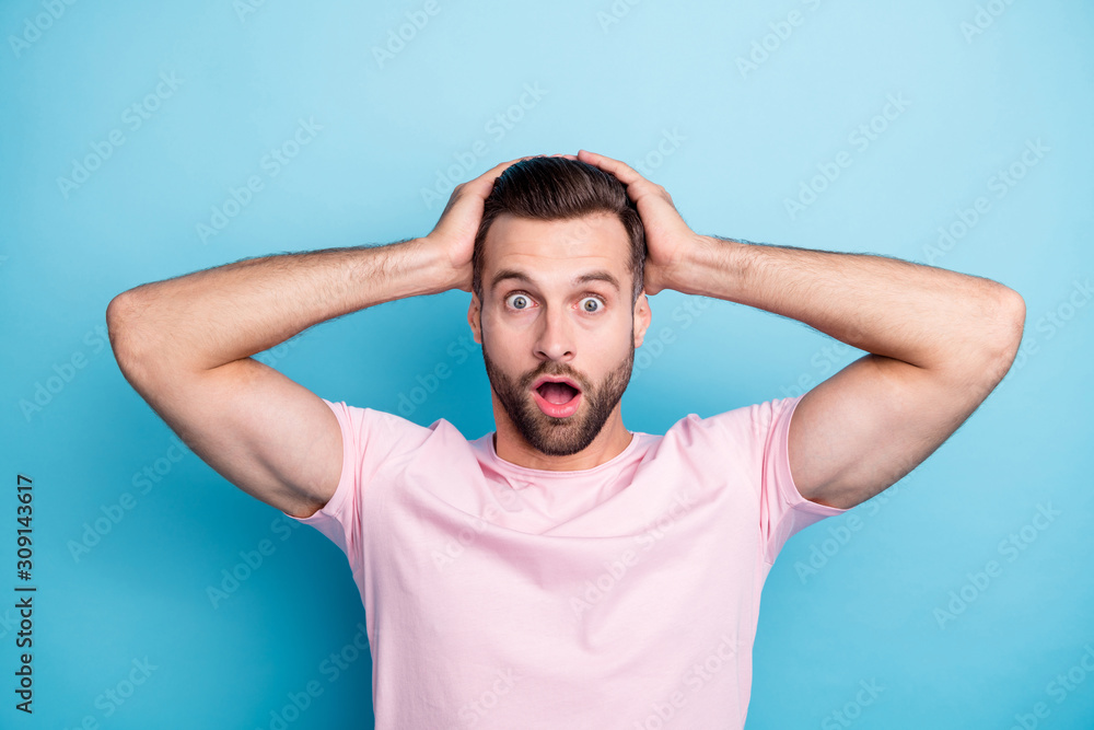 Closeup photo of amazing guy with open mouth holding arms on head not believe eyes awful terrible situation wear casual pink t-shirt isolated blue color background Closeup photo of amazing guy with open mouth holding arms on head not believe eyes awful terrible situation wear casual pink t-shirt isolated blue color background