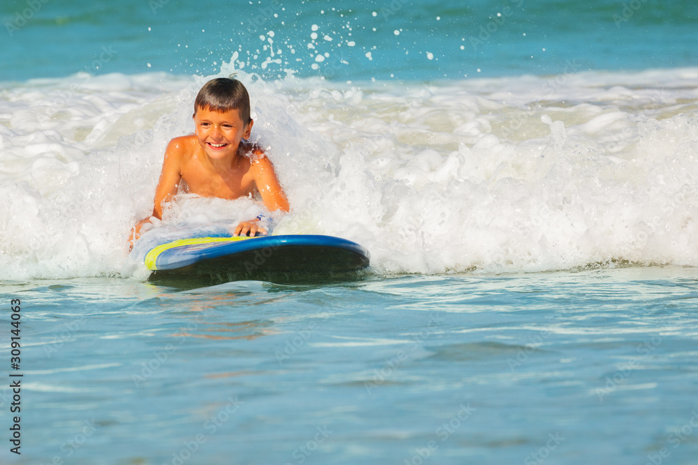 Happy smiling little boy lay on surfboard in sea