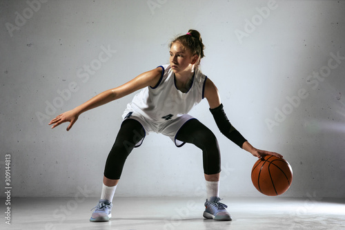 Young caucasian female basketball player of team in action, motion in run isolated on white wall background. Concept of sport, movement, energy and dynamic, healthy lifestyle. Training, practicing. © master1305