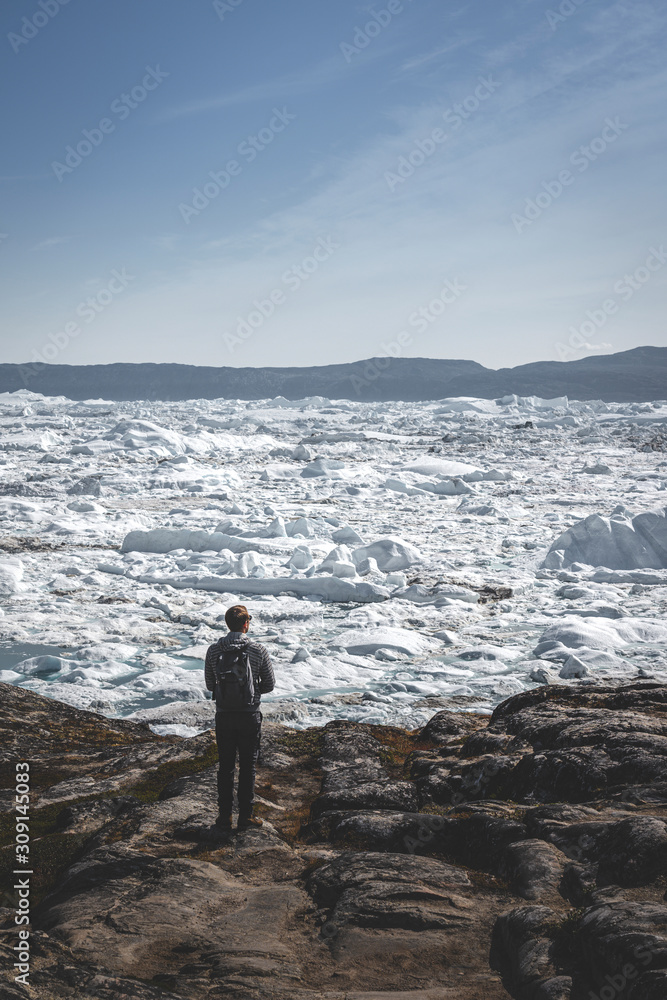 People sitting standing in front of huge glacier wall of ice. Icefjord Ilulissat. Jakobshaven Eqip Sermia Glacier Eqi glacier in Greenland called the calving glacier during midnight sun. Hikers during People sitting standing in front of huge glacier wall of ice. Icefjord Ilulissat. Jakobshaven Eqip Sermia Glacier Eqi glacier in Greenland called the calving glacier during midnight sun. Hikers during