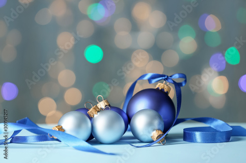Beautiful Christmas balls with ribbon on table against blurred lights