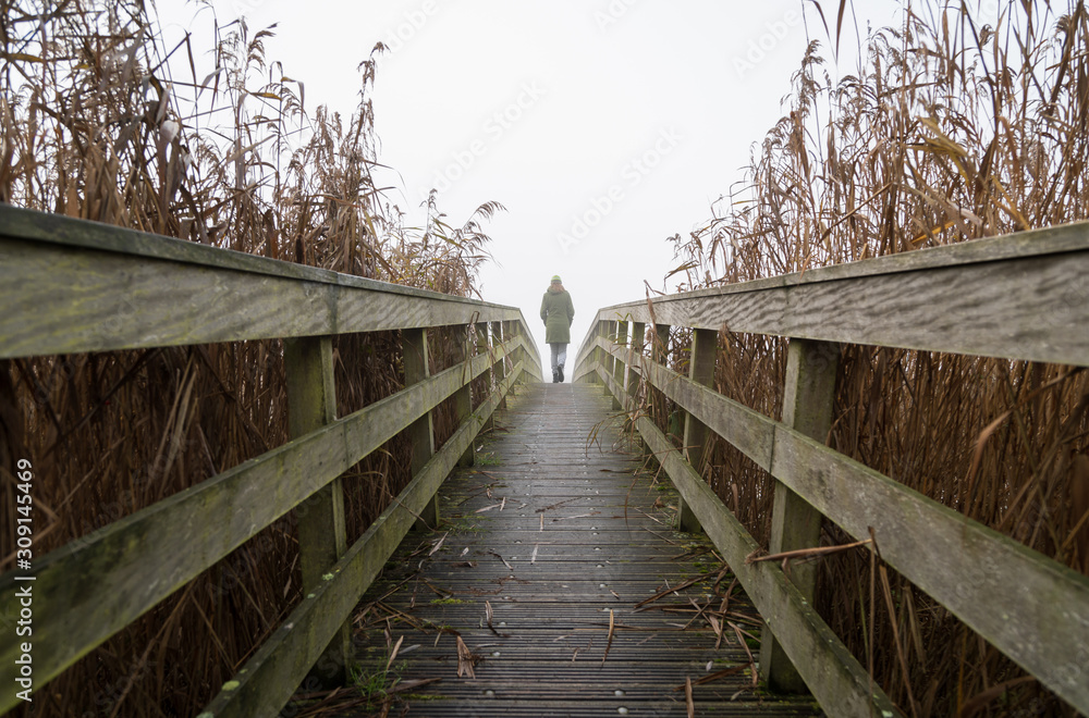 A woman walking on a small footbridge on a foggy, autumn day.