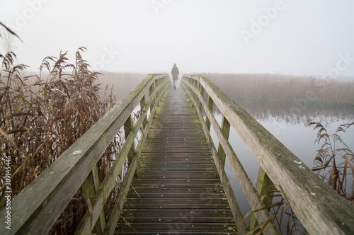 Canvas-taulu A woman walking on a small footbridge on a foggy day in autumn.
