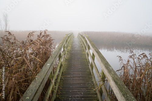 Tablou canvas Small footbridge over a river on a foggy day in autumn.