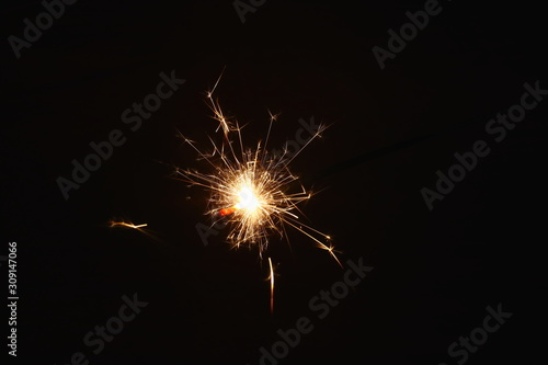 Christmas and New Year's illumination. Burning sparklers scatter bright exploding strips of sparks on a dark background. © Mikhail