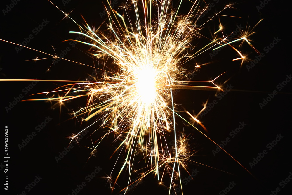 Christmas and New Year's illumination. Burning sparklers scatter bright exploding strips of sparks on a dark background.