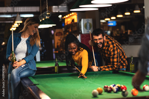 Four smiling friends in bar playing billiard together. photo