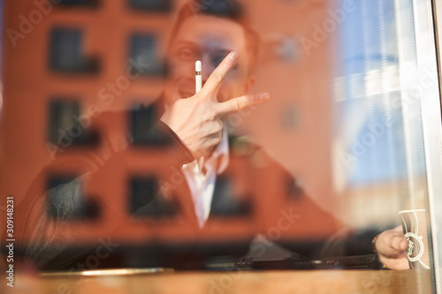 Male businessman with phone and tablet sitting in cafe, building reflection