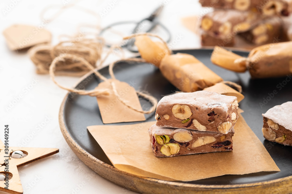 Fototapeta premium A variety of different nutty nougat in dark chocolate with roasted hazelnuts cut open to show the nougat mix on a wooden board . Copy space.
