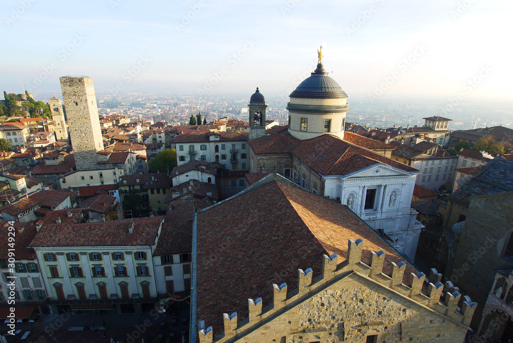 Aerial view of Bergamo old town,  roofs and cupola of cathedral, medieval tower against misty horizon. 