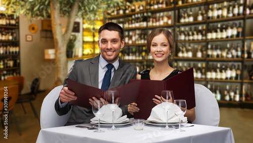leisure and luxury concept - smiling couple with menus over restaurant or wine bar background