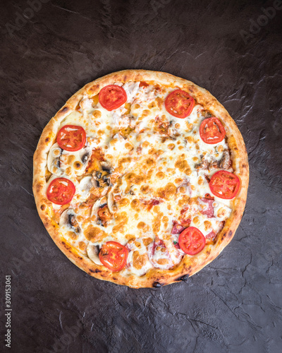 Pizza with mushrooms, tomatoes, smoked sausage and cheese on a dark background