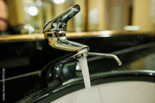 Shallow depth of field  selective focus  image with water running from a faucet and a soap dispenser in a hotel bathroom.