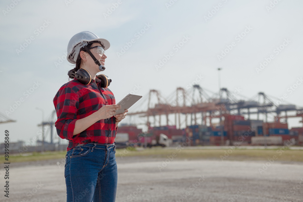 Young female engineer in protective work white wear in shipping yard examining cargo, background cargo, transport cargo engineer worker concept. Young female engineer in protective work white wear in shipping yard examining cargo, background cargo, transport cargo engineer worker concept.