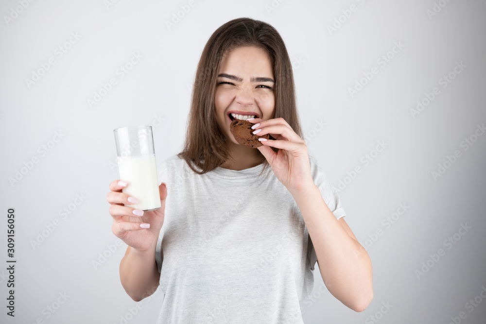young beautiful brunette woman biting chocolate cookie holding glass of milk healthy lifestyle isolated white background