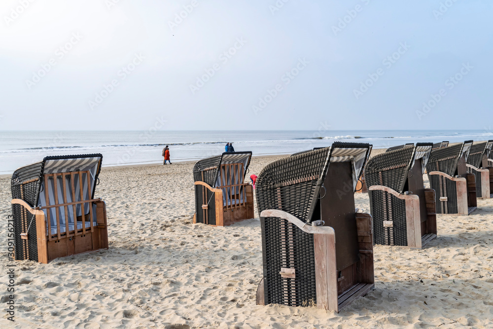 lonely cold beach with Striped cabanas sun protection chairs. people are walking at the winter or spring seashore. Egmond aan Zee, North Sea, the Netherlands lonely cold beach with Striped cabanas sun protection chairs. people are walking at the winter or spring seashore. Egmond aan Zee, North Sea, the Netherlands