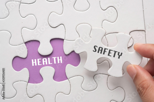 Hand hold piece of puzzle written SAFETY revealing word HEALTH. Health and Safety concept.