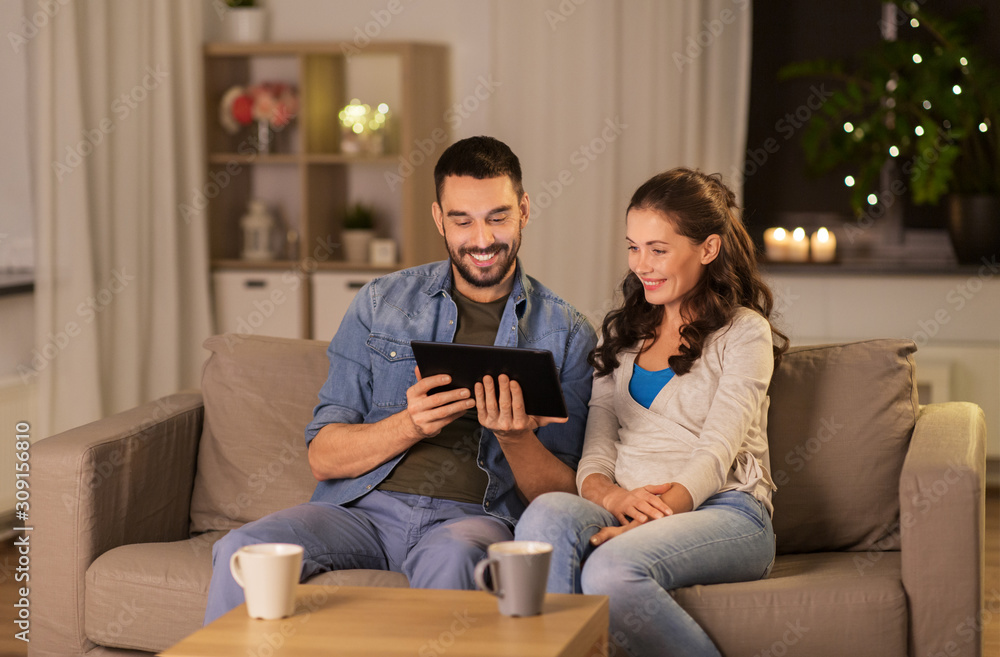 Obraz premium technology, internet and people concept - happy couple using tablet computer at home in evening