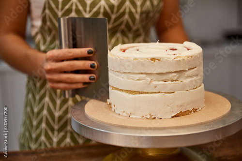Bilde på lerret Cropped view of confectioner using scraper for aligning cream on cake