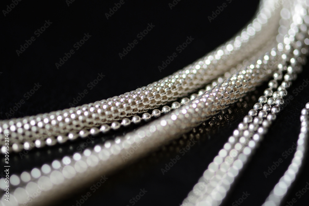 Stylish metal necklace on a black leather surface close-up. Fashion and elegance concept