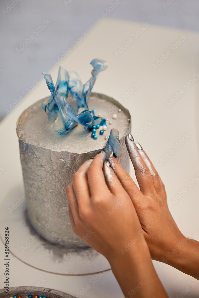 Cropped view of confectioner decorating cake on board