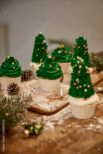 Decorated Christmas tree cupcakes with christmas balls with spruce branch and cones on table