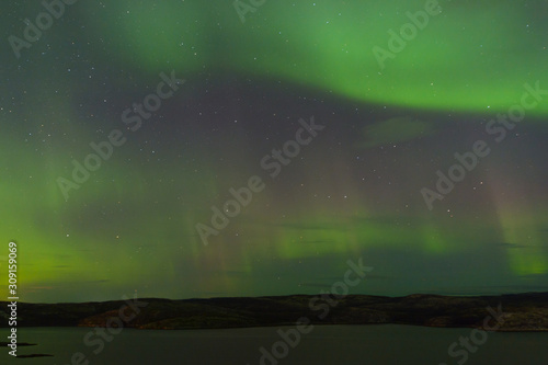 Northern lights over the lake and hills. Aurora at night in the sky in the north. © Moroshka